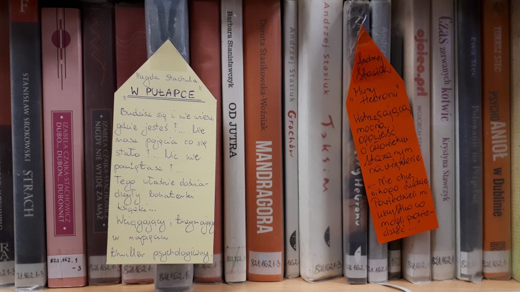 ksiązki na półce, przy dwóch książkach karteczki z opisem