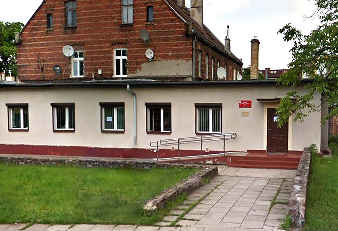 Zdjęcie przedstawia budynek filii. Budynek jest parterowy, do drzwi prowadzą schody lub podjazd dla osób z niepełnosprawnością. przed budynkiem jest mały teren z trawą.