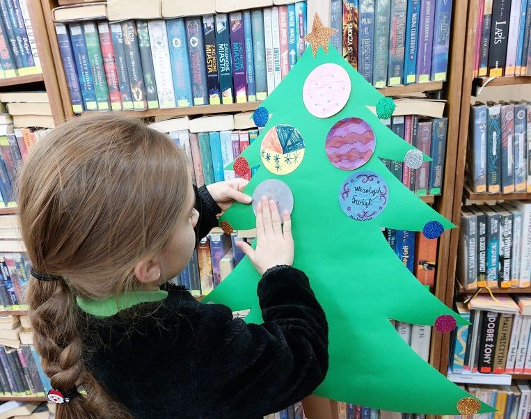 Dziewczynka trzymająca choinkę z papieru na tle regału z książkami