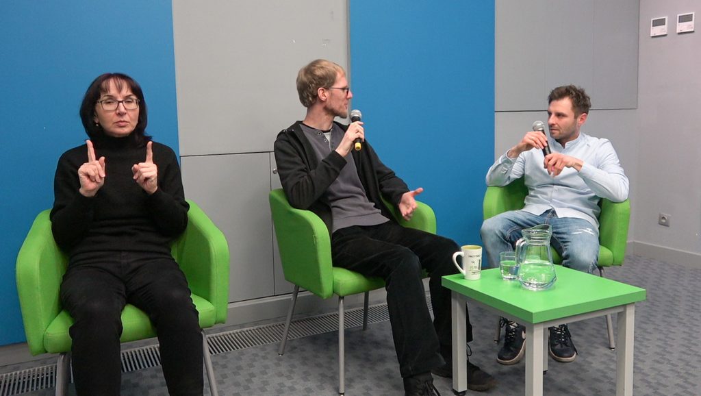 Prowadzący spotkanie w rozmowie z gościem. Po lewej stornie Pani tłumacząca na język migowy